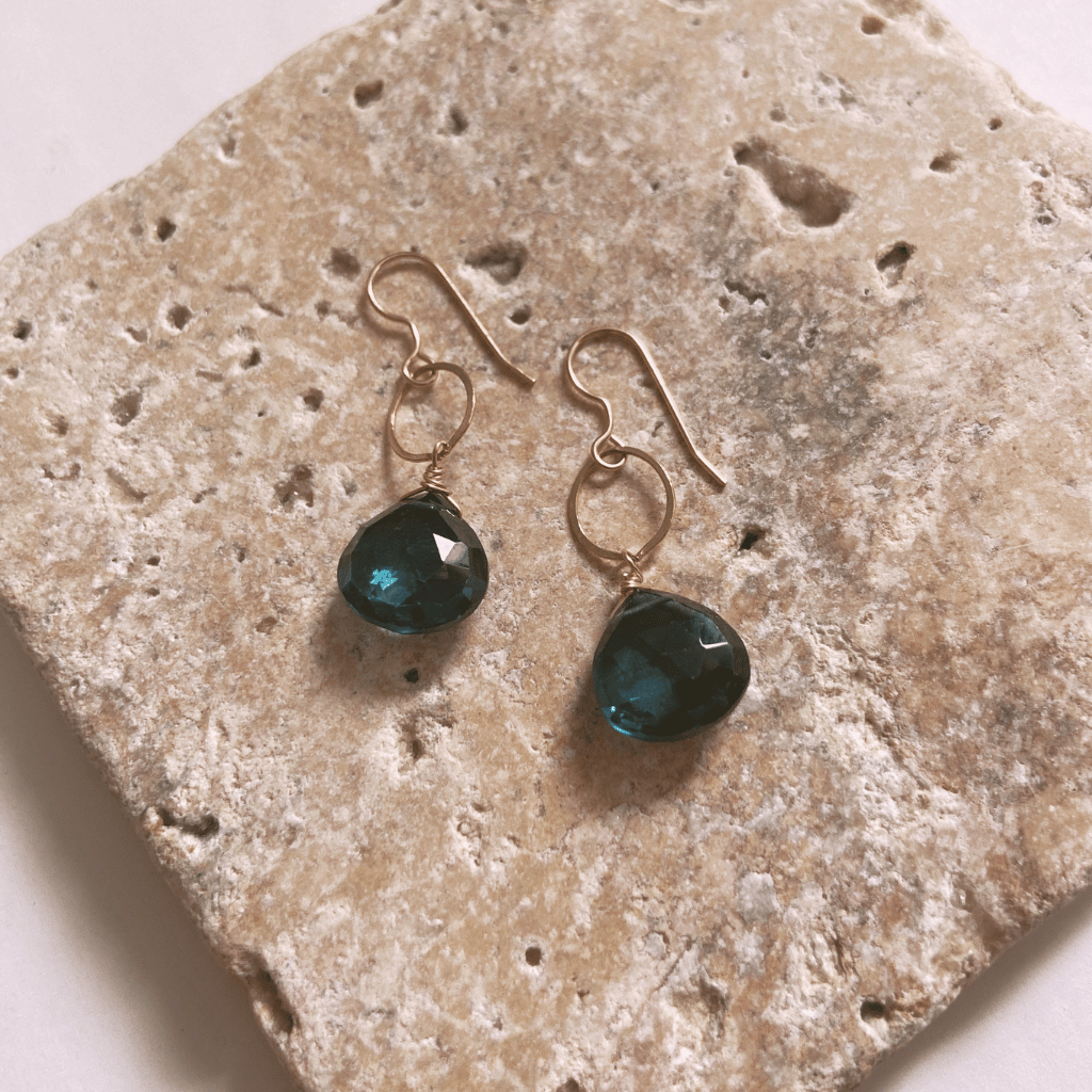 Gold earrings with green gemstones on a textured stone surface