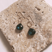 Gold earrings with green gemstones on a textured stone surface